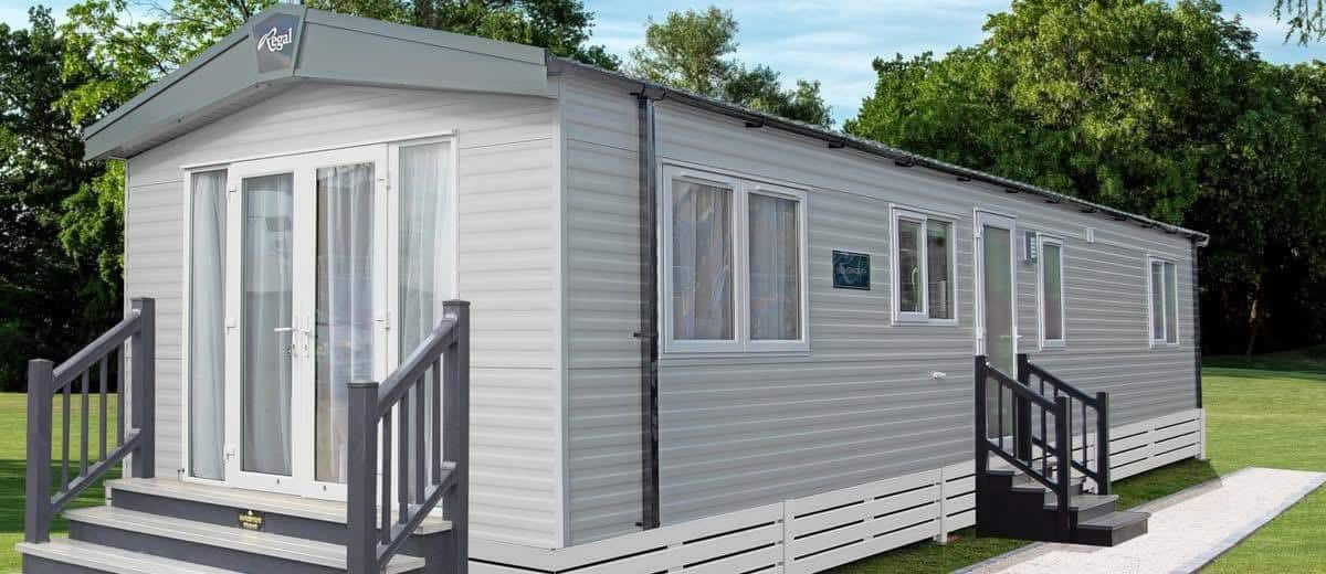 The outside of a new Regal static caravan, with grey cladding and steps up to French doors